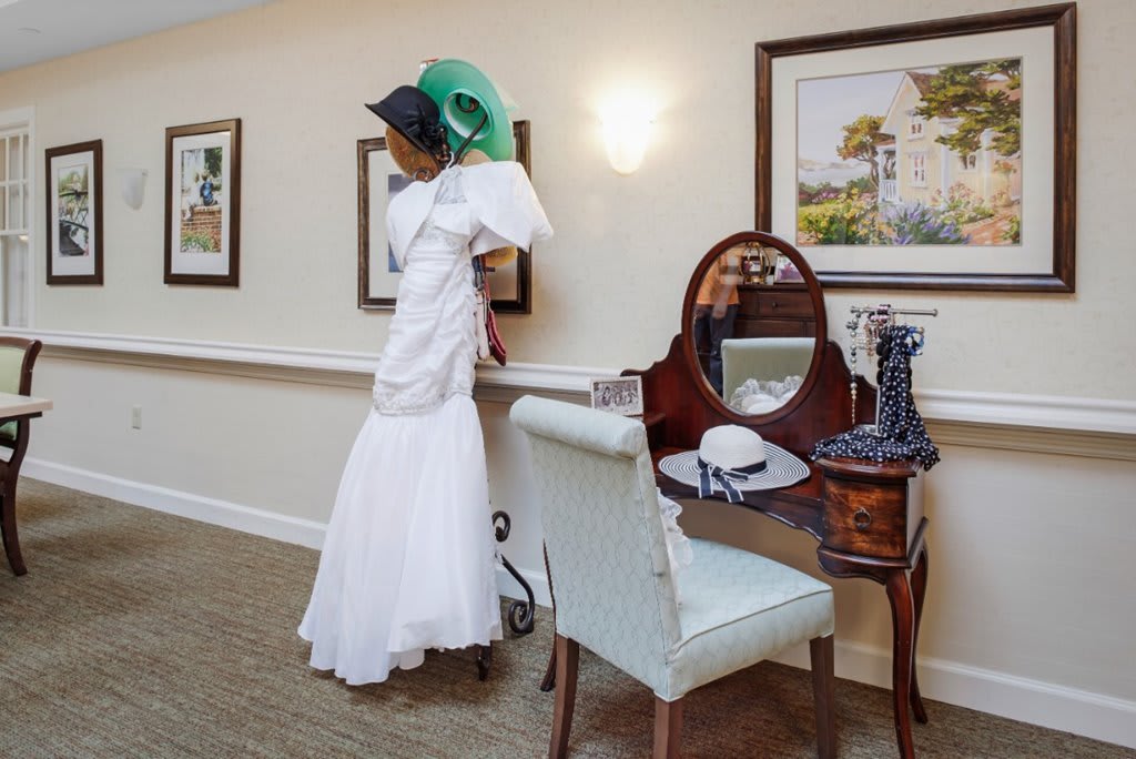 A mannequin dressed in a vintage white gown and green hat stands beside a classic vanity table.