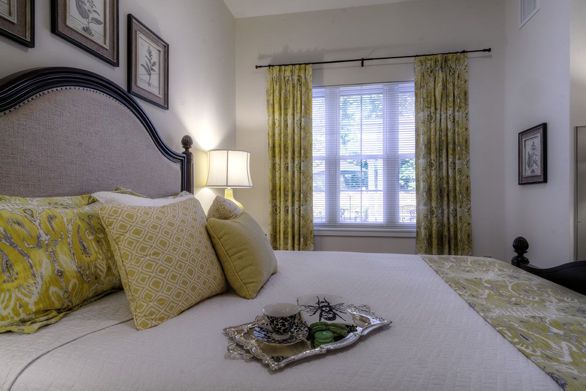 A cozy bedroom with a neatly made bed, adorned with pillows and a breakfast tray, illuminated by soft lamp light.