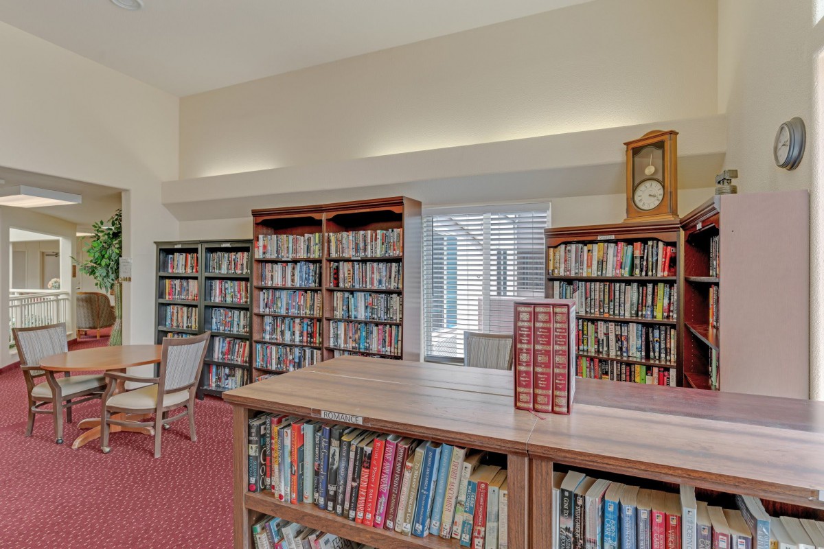 A quiet library room with bookshelves filled with books, a reading table, and a clock on the wall.