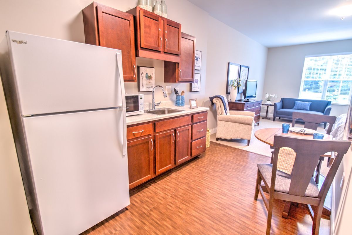 A cozy kitchen area with wooden cabinets, a refrigerator, and a view into a connected living space.