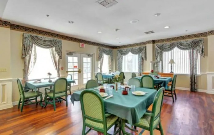 A cozy dining room with neatly arranged tables and chairs, featuring elegant curtains and a wooden floor.