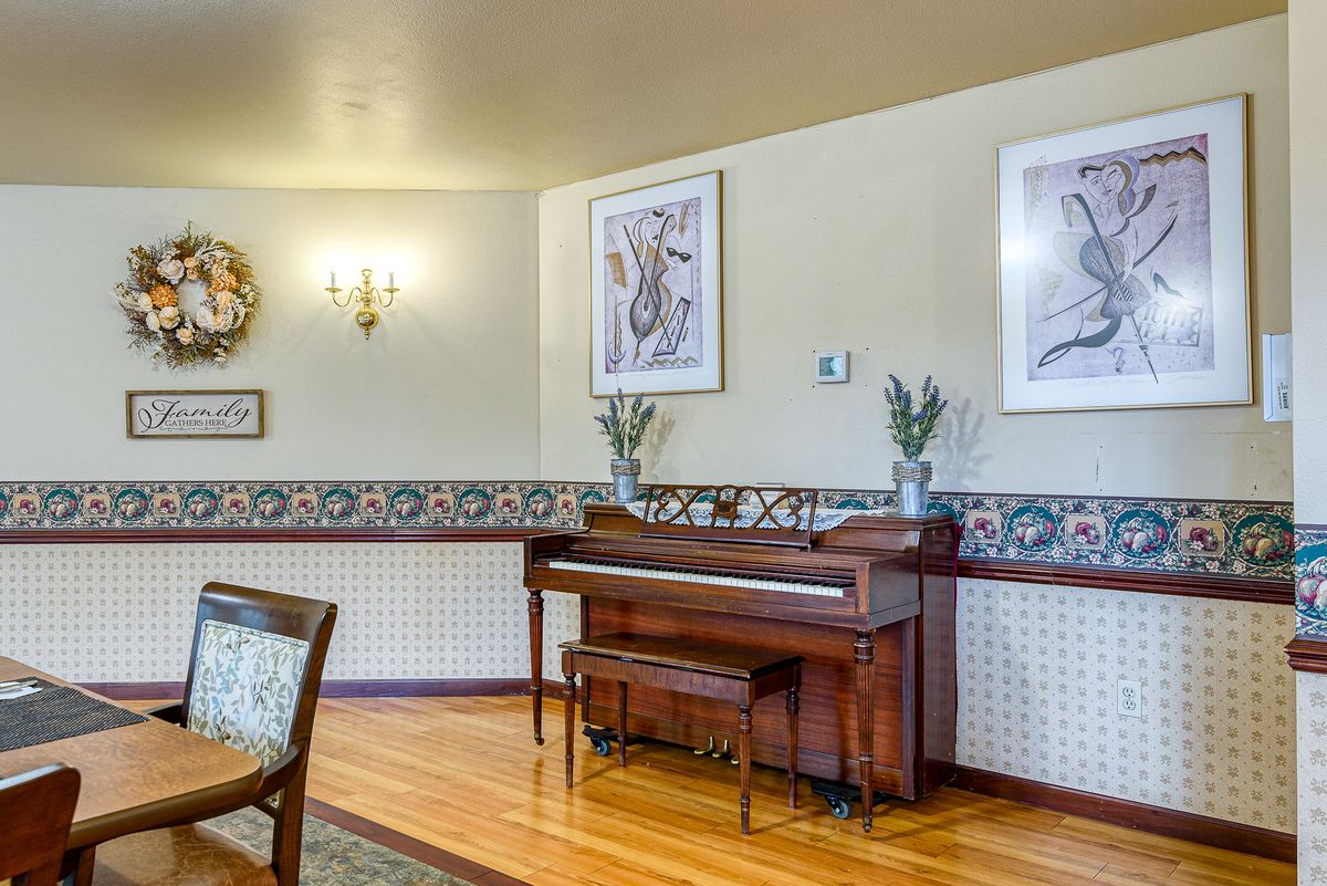 A cozy living room features a wooden piano against an artistically decorated wall, complete with framed artwork and elegant lighting.