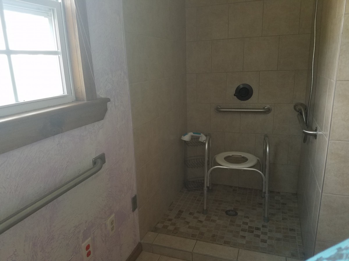 An accessible bathroom with a shower chair and grab bars.