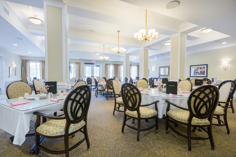 An elegant dining room with neatly arranged tables and chairs, illuminated by chandeliers.