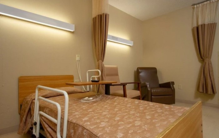 A hospital room with a bed, chairs, and a privacy curtain.