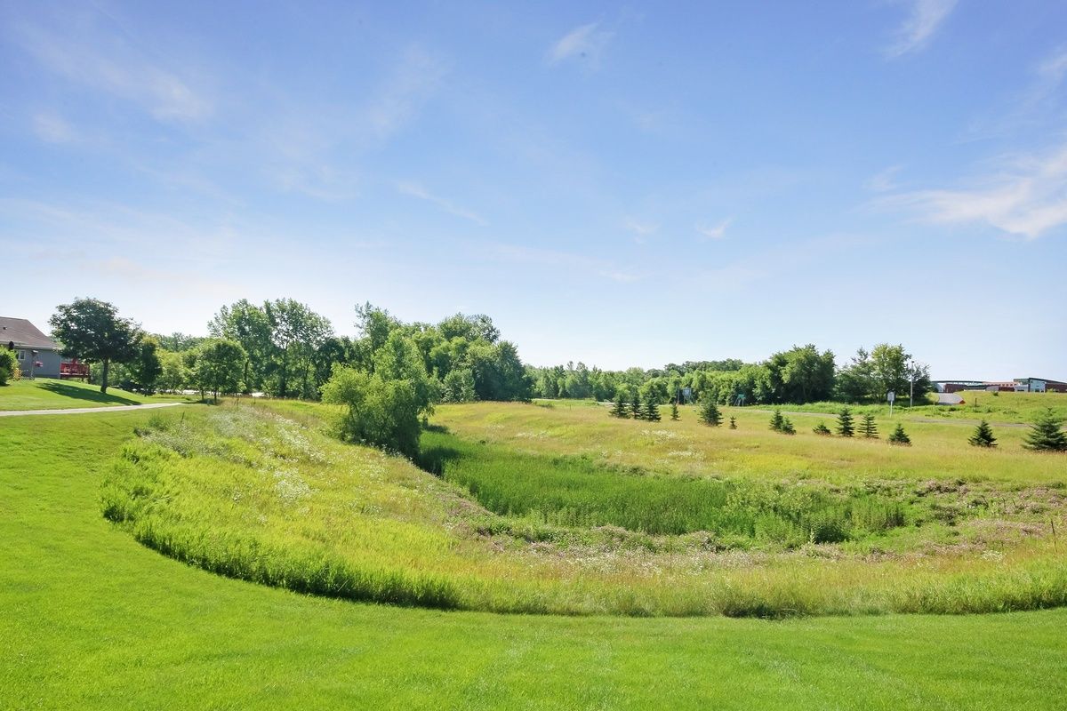 A scenic view of a lush green field with trees under a clear blue sky.