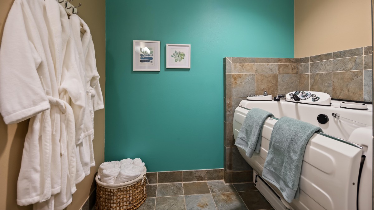 A well-decorated bathroom featuring a turquoise wall, framed artwork, and neatly arranged towels beside a tiled bathtub.