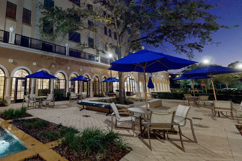 A night view of an outdoor patio with blue umbrellas and seating in front of a building.