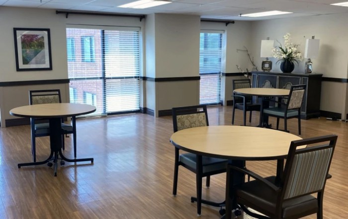 An empty room with round tables and chairs, featuring large windows.