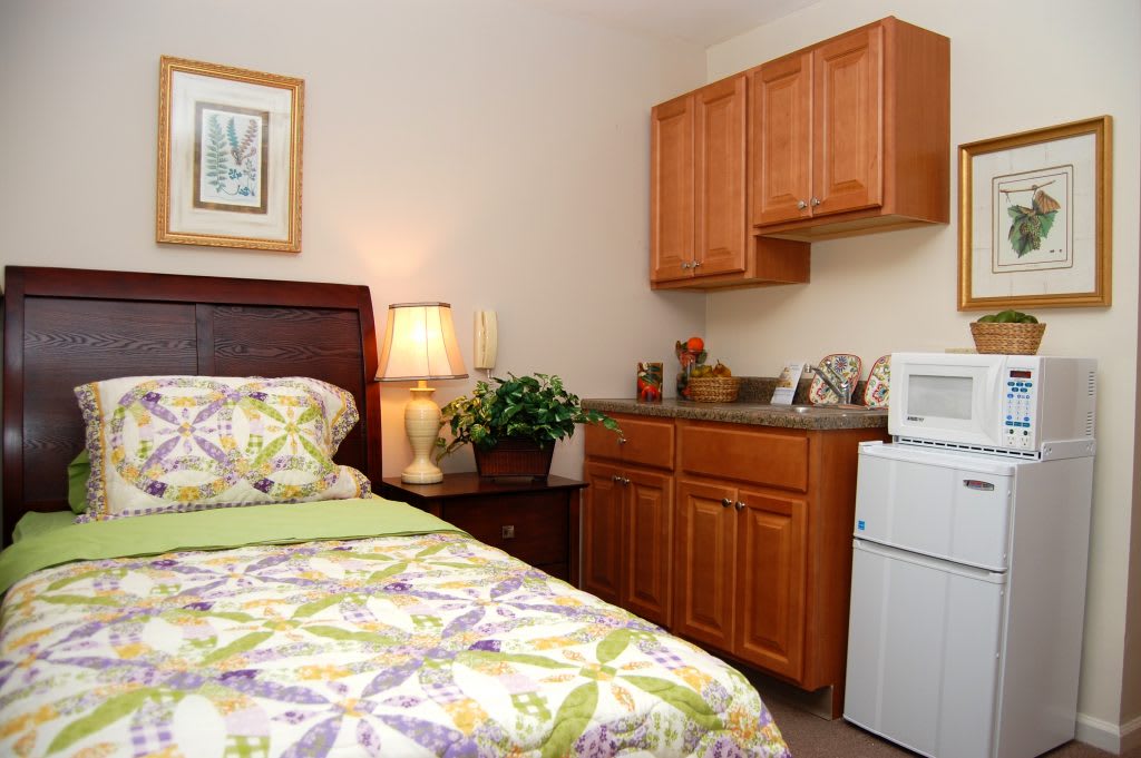 A cozy bedroom with a single bed, wooden cabinets, and a small fridge.