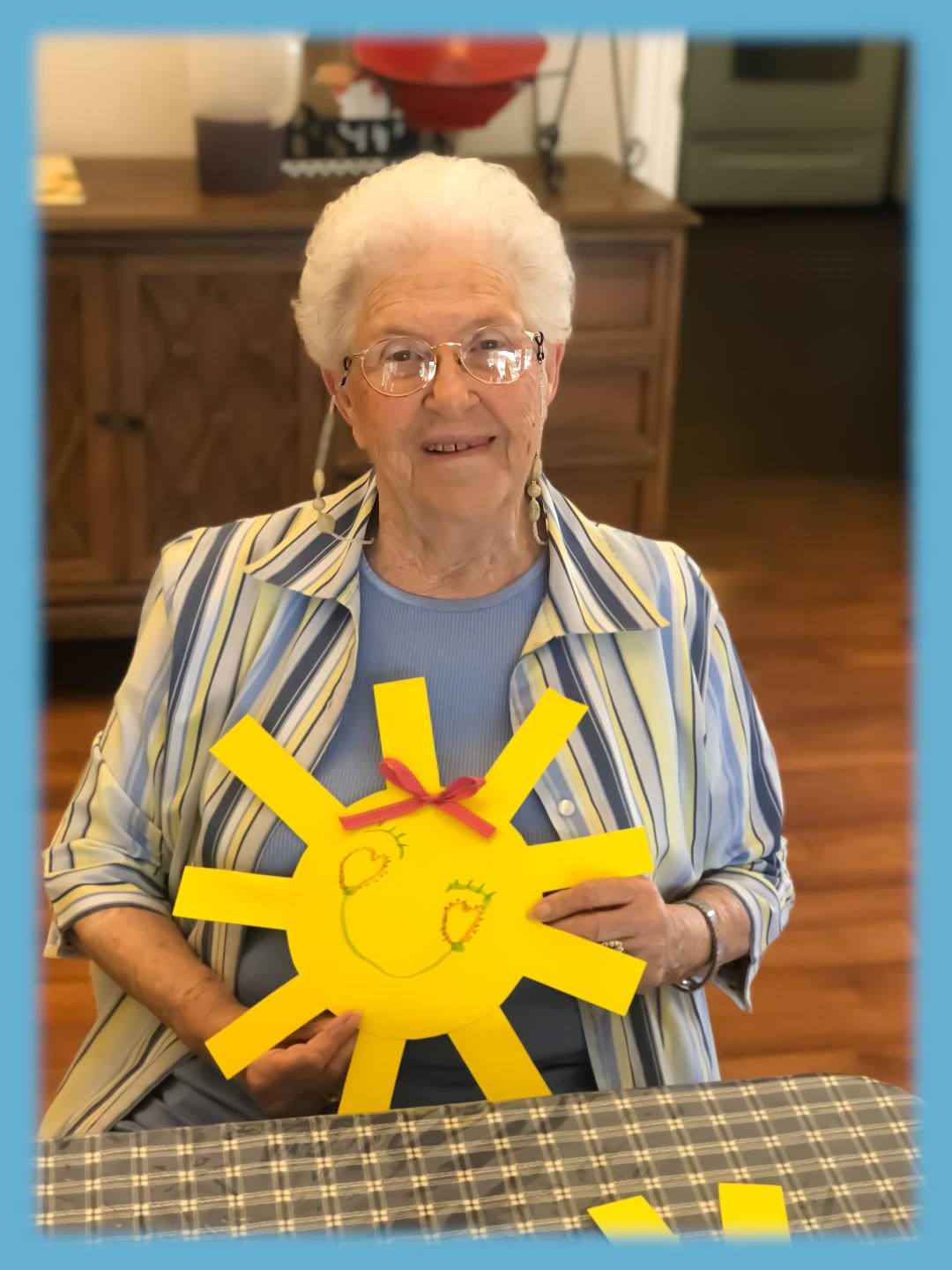 An elderly woman proudly displays her handmade craft depicting a sun.