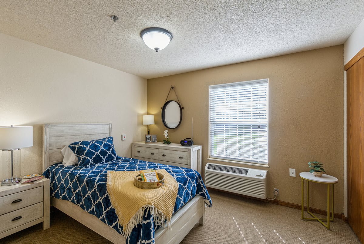 A cozy bedroom with a neatly made bed, a dresser with a mirror, and a lamp near the window.
