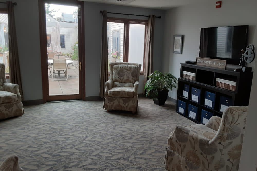 A cozy living room with armchairs, a TV stand, and large windows allowing natural light.