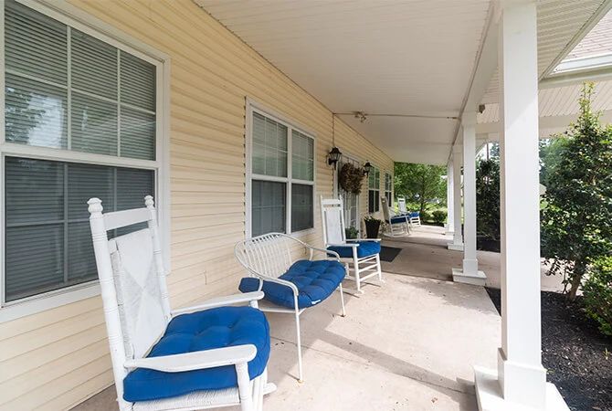 A cozy porch featuring white rocking chairs with blue cushions, surrounded by windows and hanging plants.
