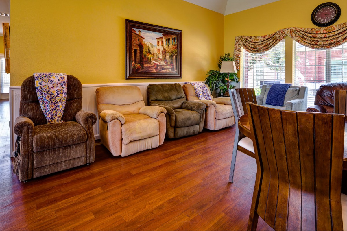 A cozy living room with a row of recliners, hardwood floors, and a dining area.