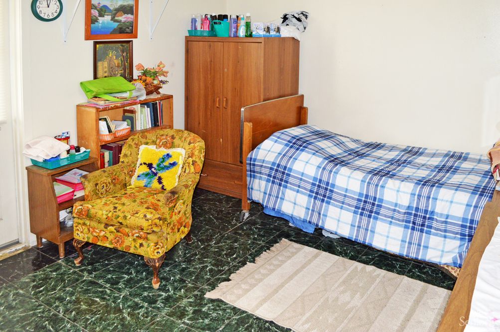 A cozy bedroom with a single bed, vintage armchair, and bookshelf.