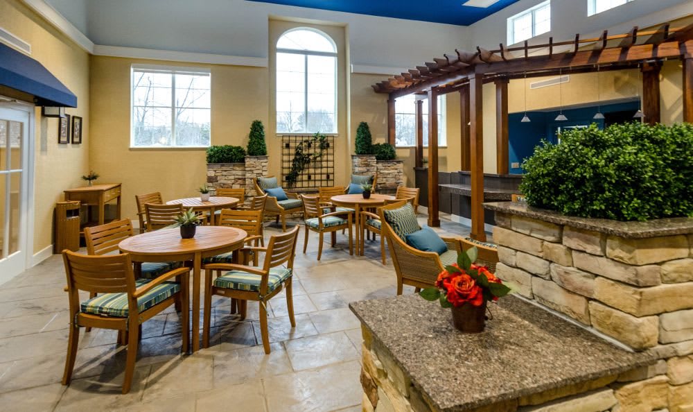 A well-lit indoor seating area with wooden tables and chairs, surrounded by decorative plants.