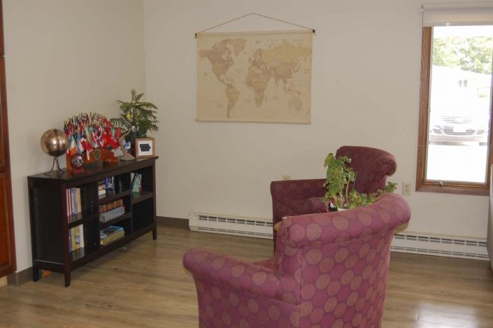 A cozy office seating area with two chairs, a world map on the wall, and a shelf with books and plants.