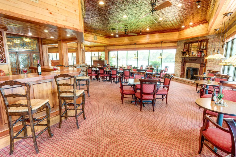 A warm and inviting restaurant interior featuring wooden decor, with tables and chairs arranged on a carpeted floor alongside a cozy fireplace.