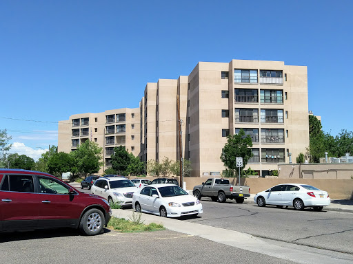A street view featuring modern apartment buildings alongside parked cars under a clear blue sky.