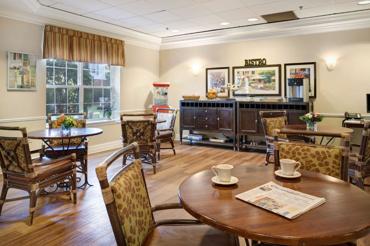 A cozy indoor cafe with wooden tables and chairs, featuring decorative art on the walls and a window letting in natural light.