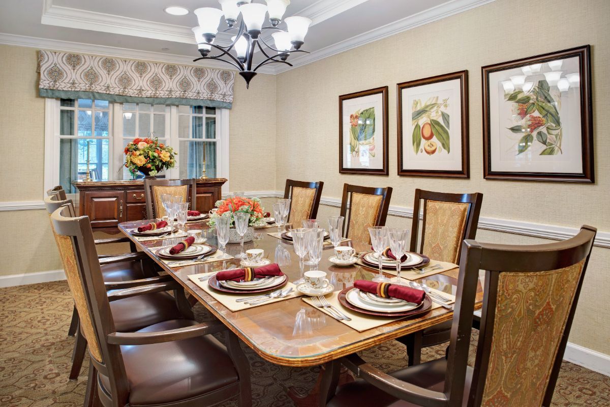A beautifully set dining table in an elegant dining room with a chandelier, artwork on the walls, and floral centerpieces.