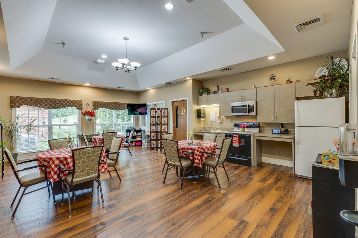 A spacious and modern dining area with a kitchen, featuring wood flooring and elegant lighting.