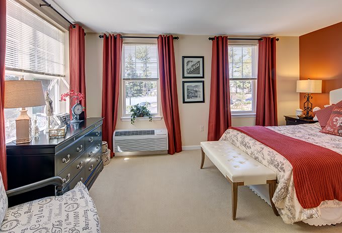 A cozy bedroom with red curtains and large windows.