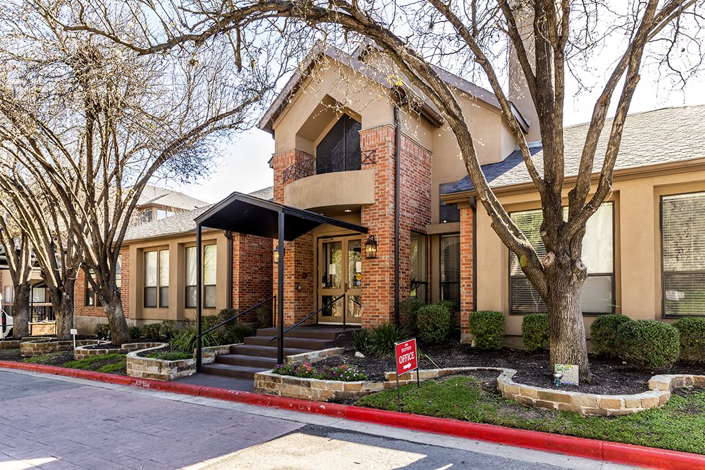 A residential building entrance with trees and landscaping.