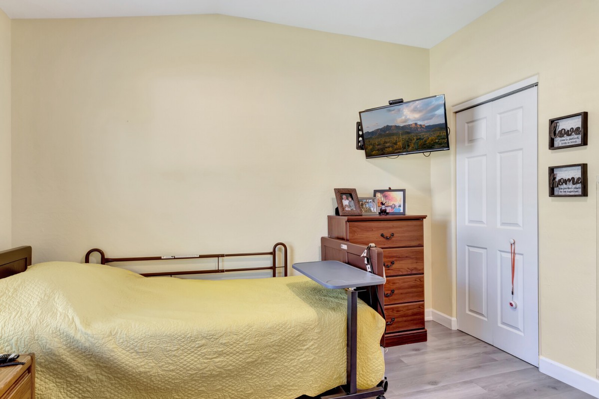 A cozy bedroom featuring a single bed with yellow sheets, a wooden dresser, and a wall-mounted TV.