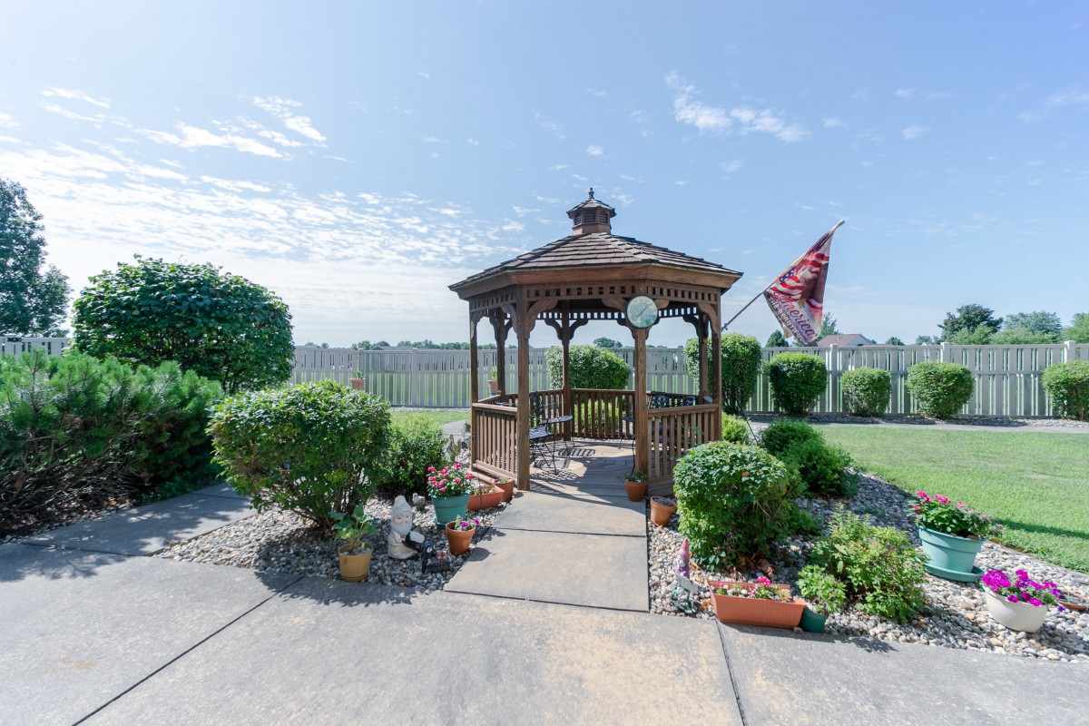 A wooden gazebo surrounded by a landscaped garden with decorative plants and an American flag in the background.