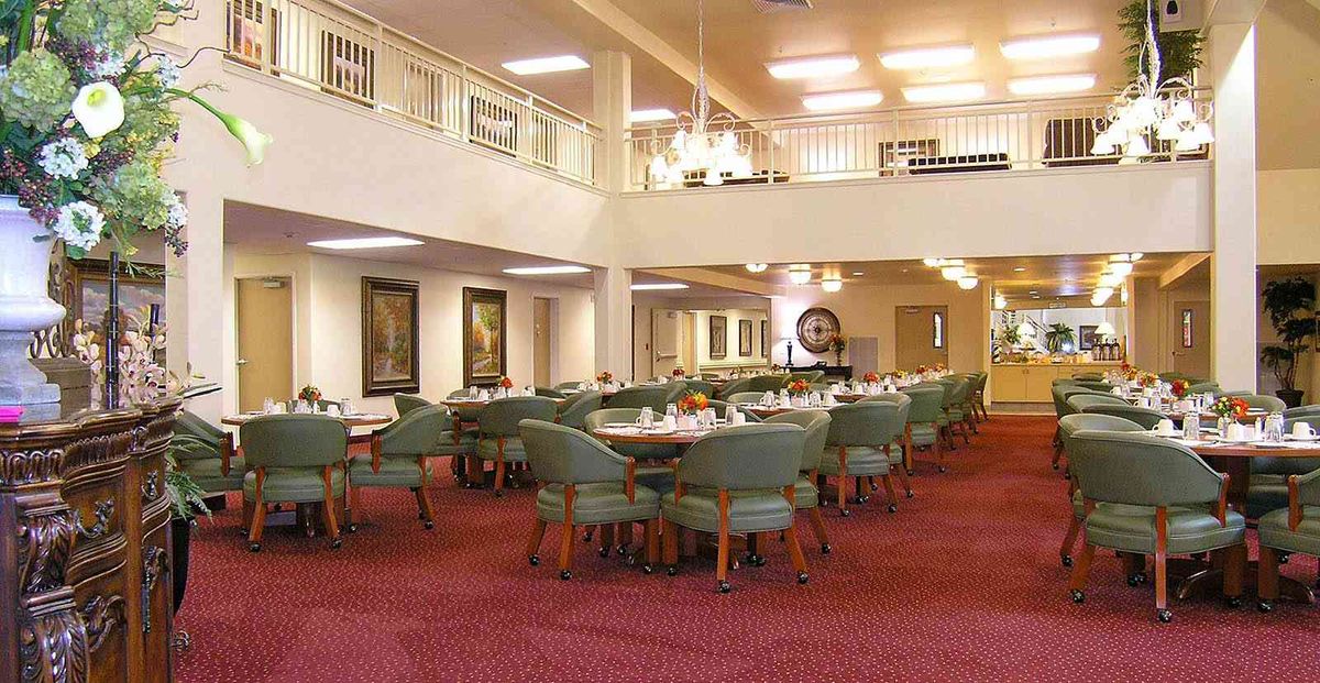A spacious dining room with multiple tables and chairs, adorned with chandeliers and elegant decor.