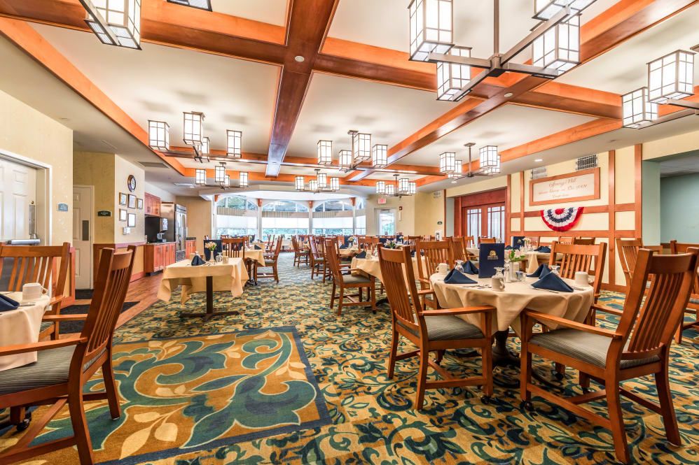 A spacious restaurant interior with elegant chandeliers, neatly arranged tables, and a patterned carpet.