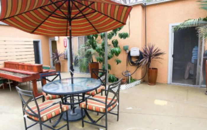 A cozy outdoor patio with a table and chairs under an umbrella, surrounded by plants.