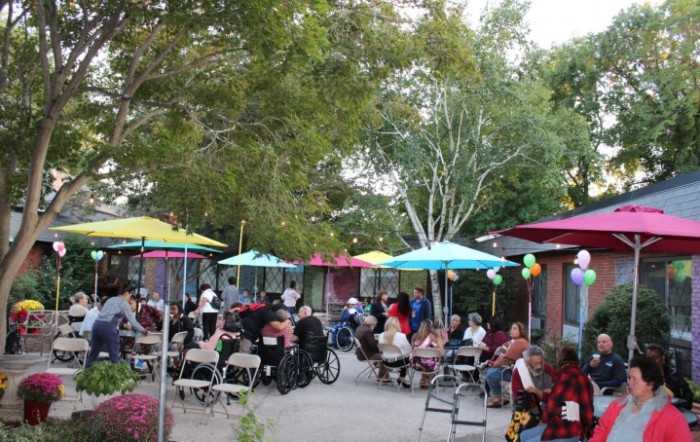 A lively outdoor gathering with people seated under colorful umbrellas.