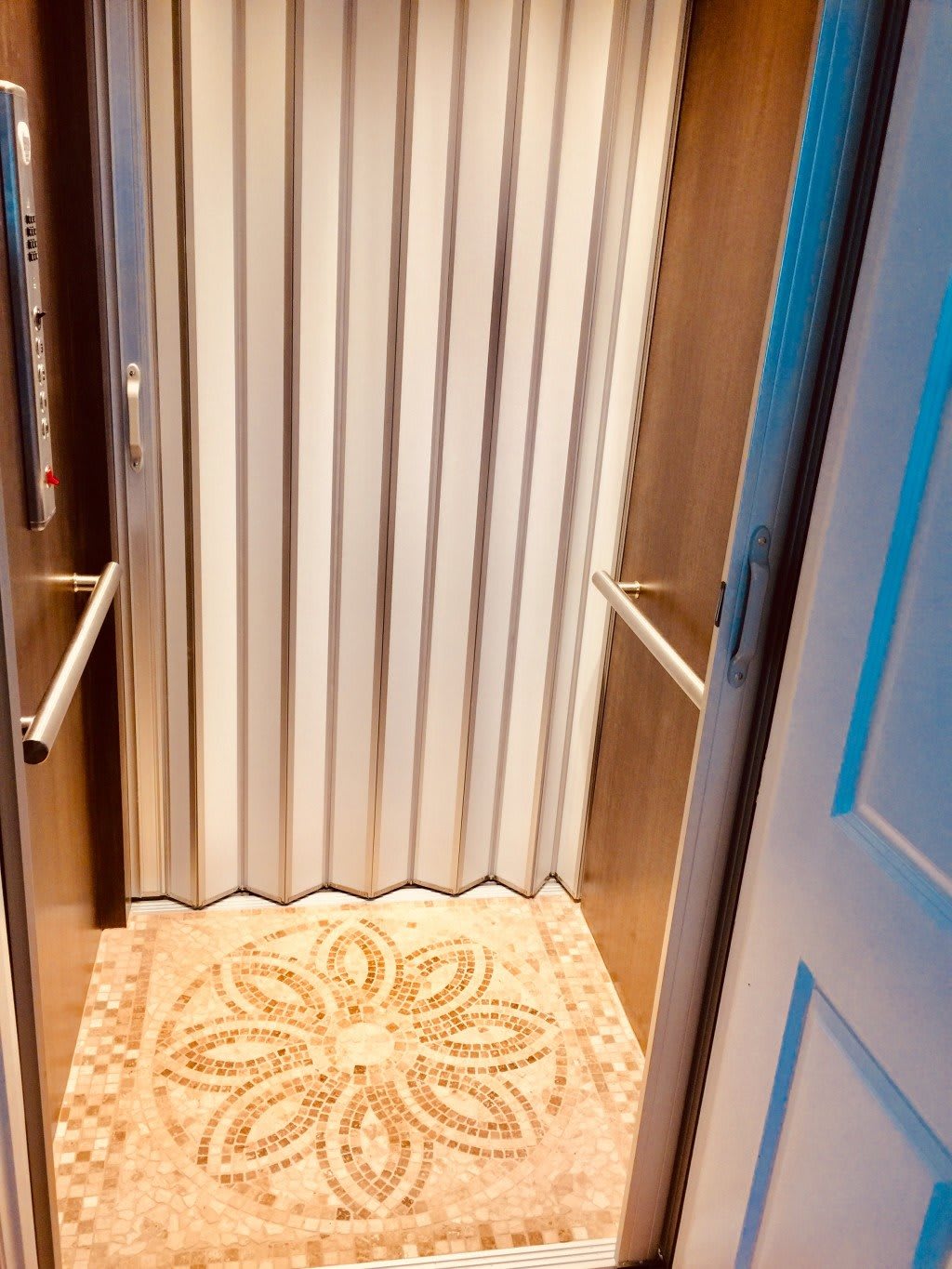 An interior view of an elevator with a folding door and patterned flooring.