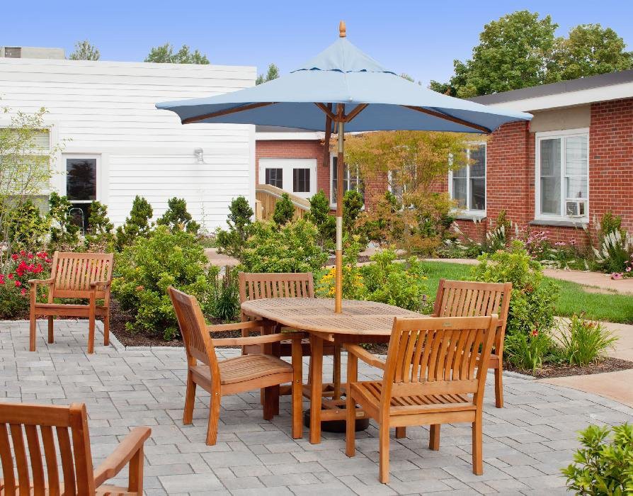 An inviting outdoor patio with wooden furniture and a large umbrella, surrounded by lush greenery.