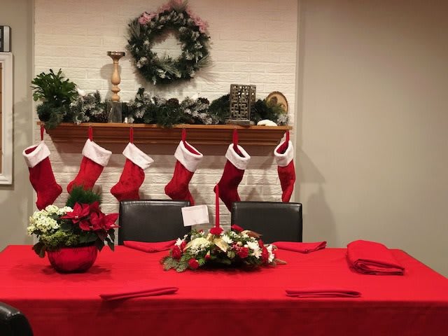 A festive Christmas setup with stockings hanging over a mantel and a table adorned with a red tablecloth and floral centerpiece.