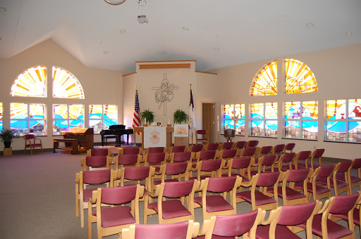 A serene interior view of a chapel with rows of chairs and colorful stained glass windows.
