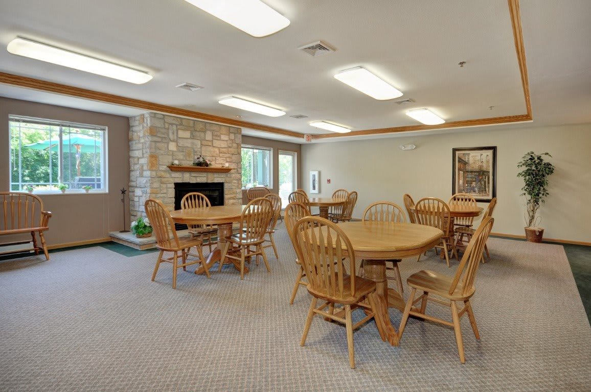A cozy dining area with wooden tables and chairs, featuring a stone fireplace and large windows.