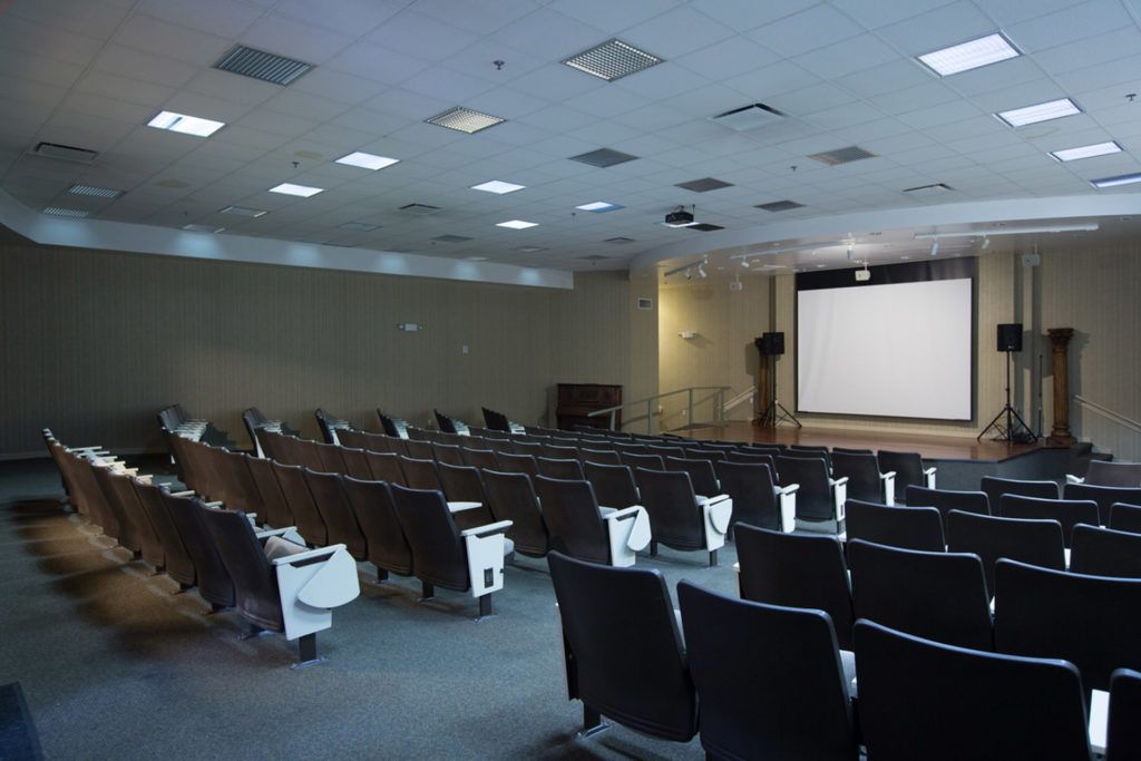 An empty auditorium with rows of seats facing a large screen.