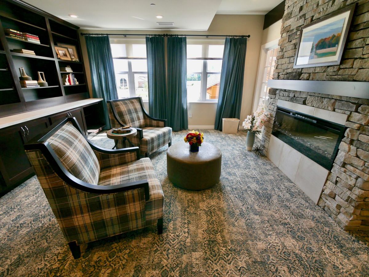 A cozy living room featuring plaid chairs, a modern fireplace, and large windows with curtains.