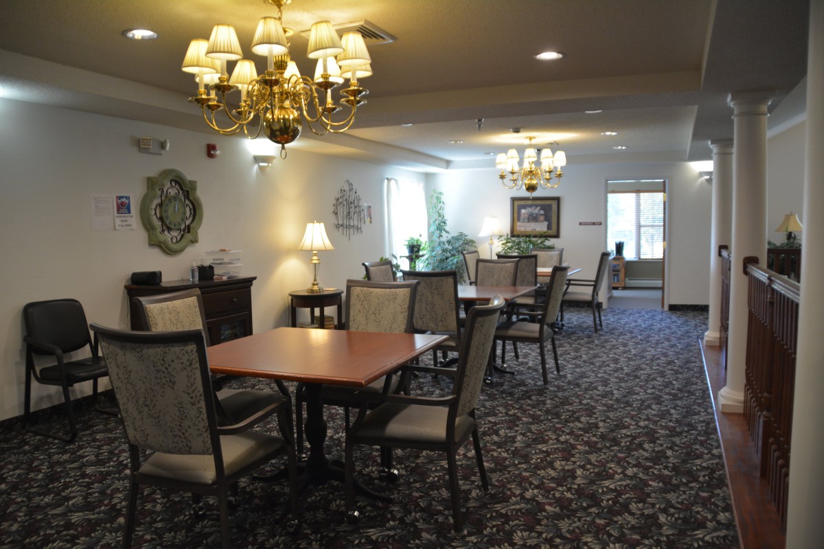 A well-lit dining room with multiple tables and chairs, featuring chandeliers and decorative elements.