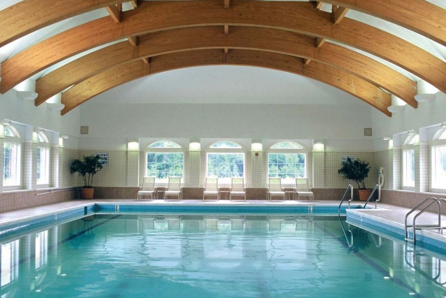 A serene indoor swimming pool with an arched wooden ceiling and large windows letting in natural light.