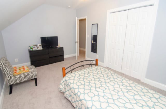 A neatly arranged bedroom with a bed, dresser, television, and closet.