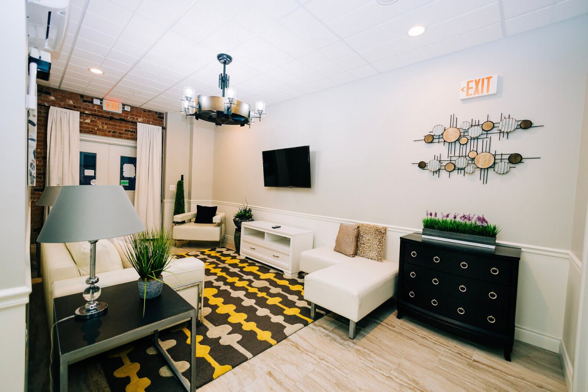 A modern living room with white furniture, a patterned carpet, and a wall-mounted television.
