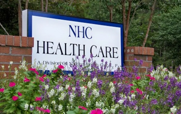 A sign for NHC Health Care surrounded by colorful flowers.