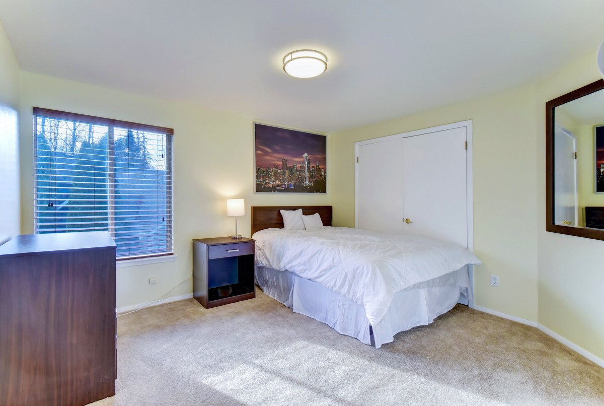 A cozy bedroom with a neatly made bed, nightstand, and a window letting in natural light.