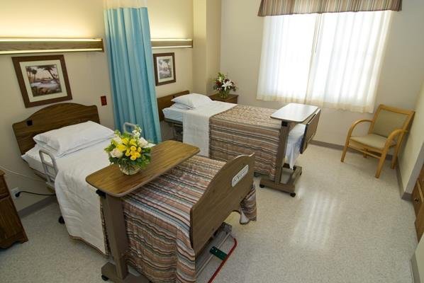 A hospital room with two beds, separated by a curtain, and a bedside table with flowers.
