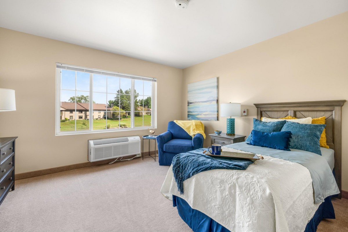 A modern and bright bedroom with blue accents and a large window offering an outdoor view.